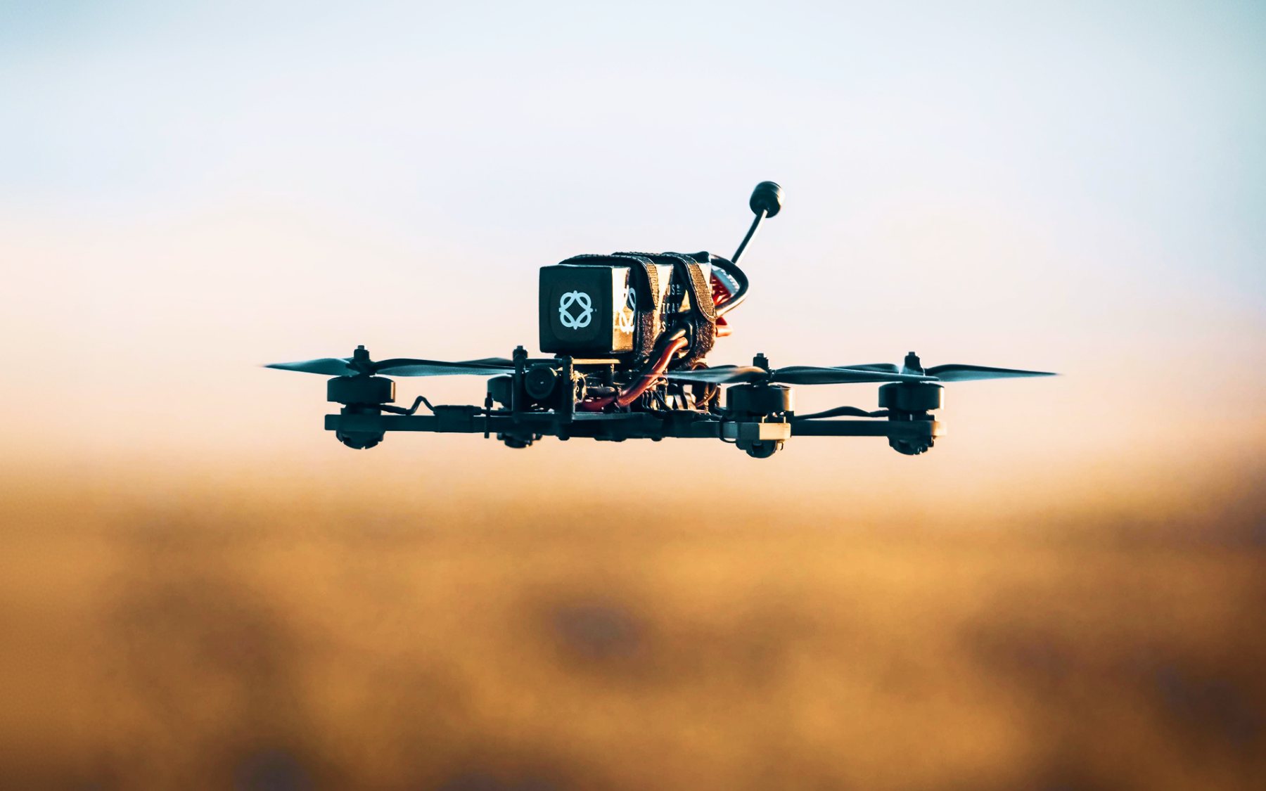 Matrix quadcopter hovering at low altitude over open ground at dusk